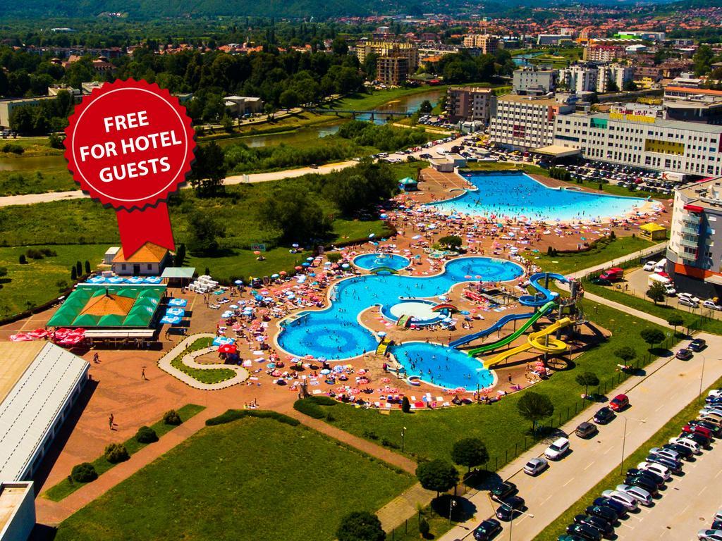 Hotel Hills Sarajevo Congress & Thermal Spa Resort Илиджа Экстерьер фото The photo shows an aerial view of a large swimming pool area, likely part of a hotel or resort. There are several pools of different shapes and sizes, including one that resembles a Mickey Mouse shape. The area is filled with numerous sun loungers an